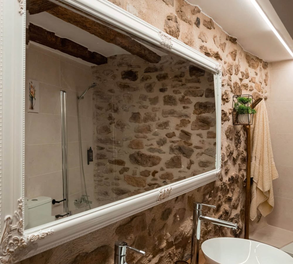 Espejo en baño con pared de piedra y ducha.