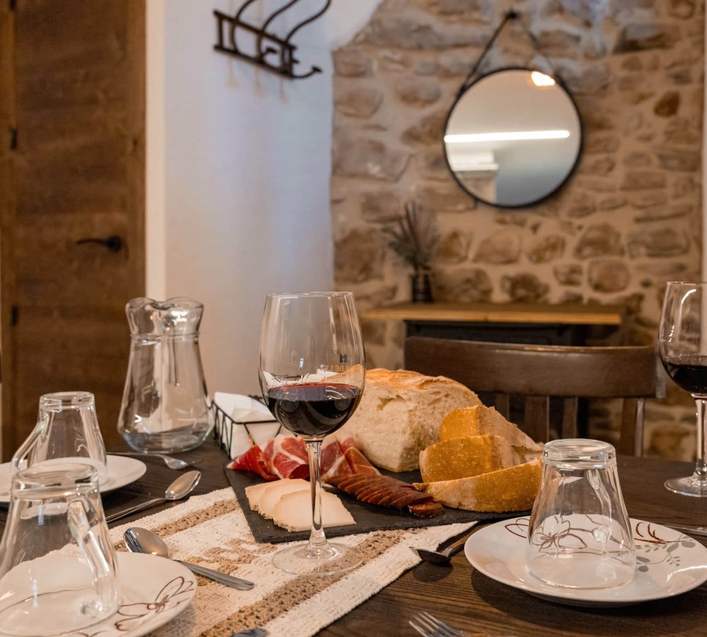 Mesa con vino, pan y embutidos en un comedor.