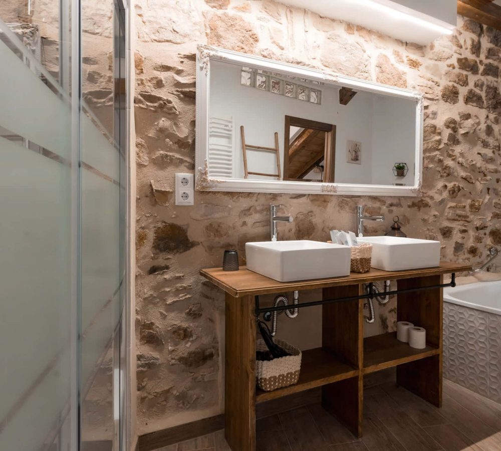 Baño moderno con paredes de piedra y doble lavabo.